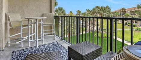 A balcony with a white chair, a small table, and a patterned rug.