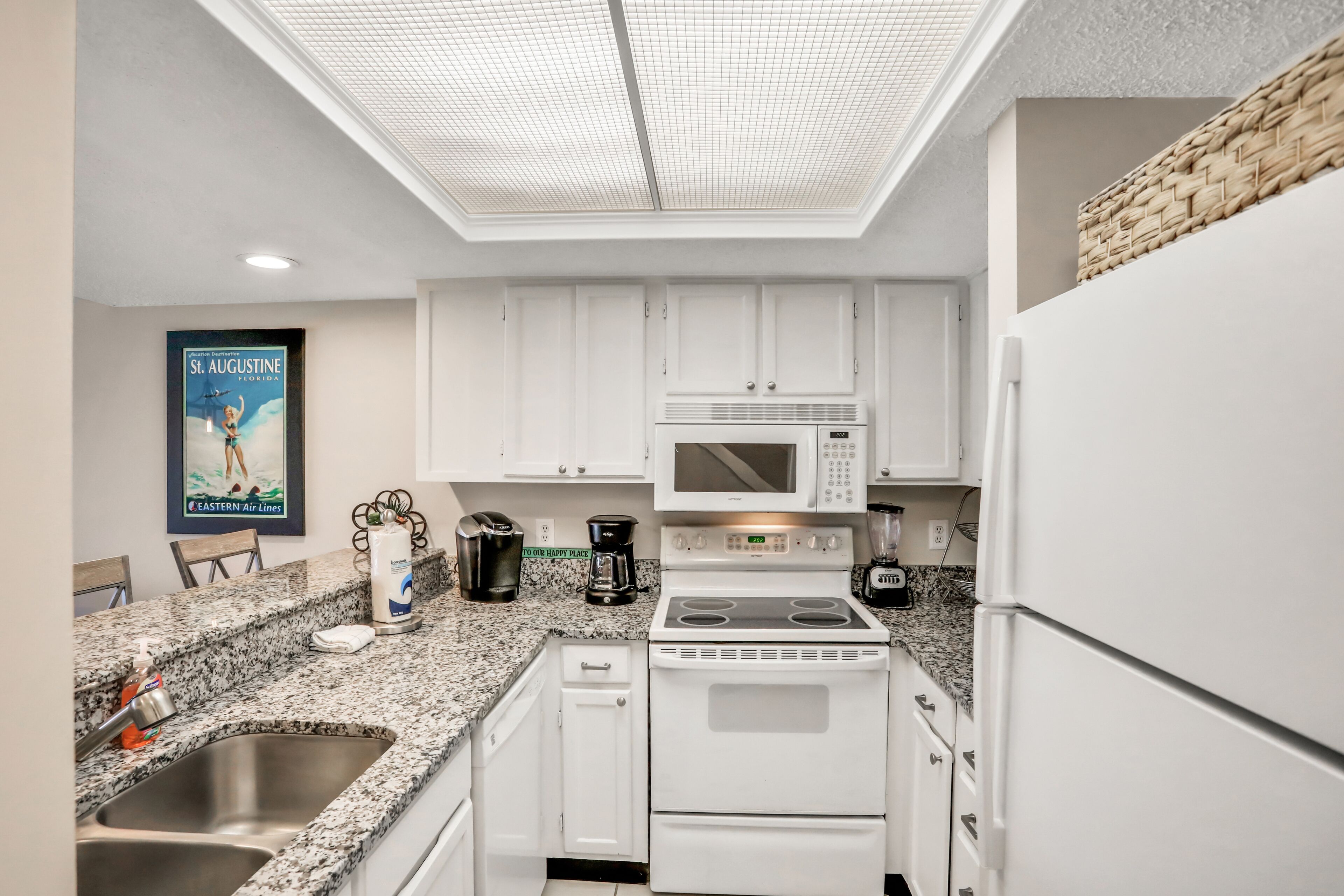 A modern kitchen with white cabinets, a stainless steel sink, a microwave, a stove, and a coffee maker.