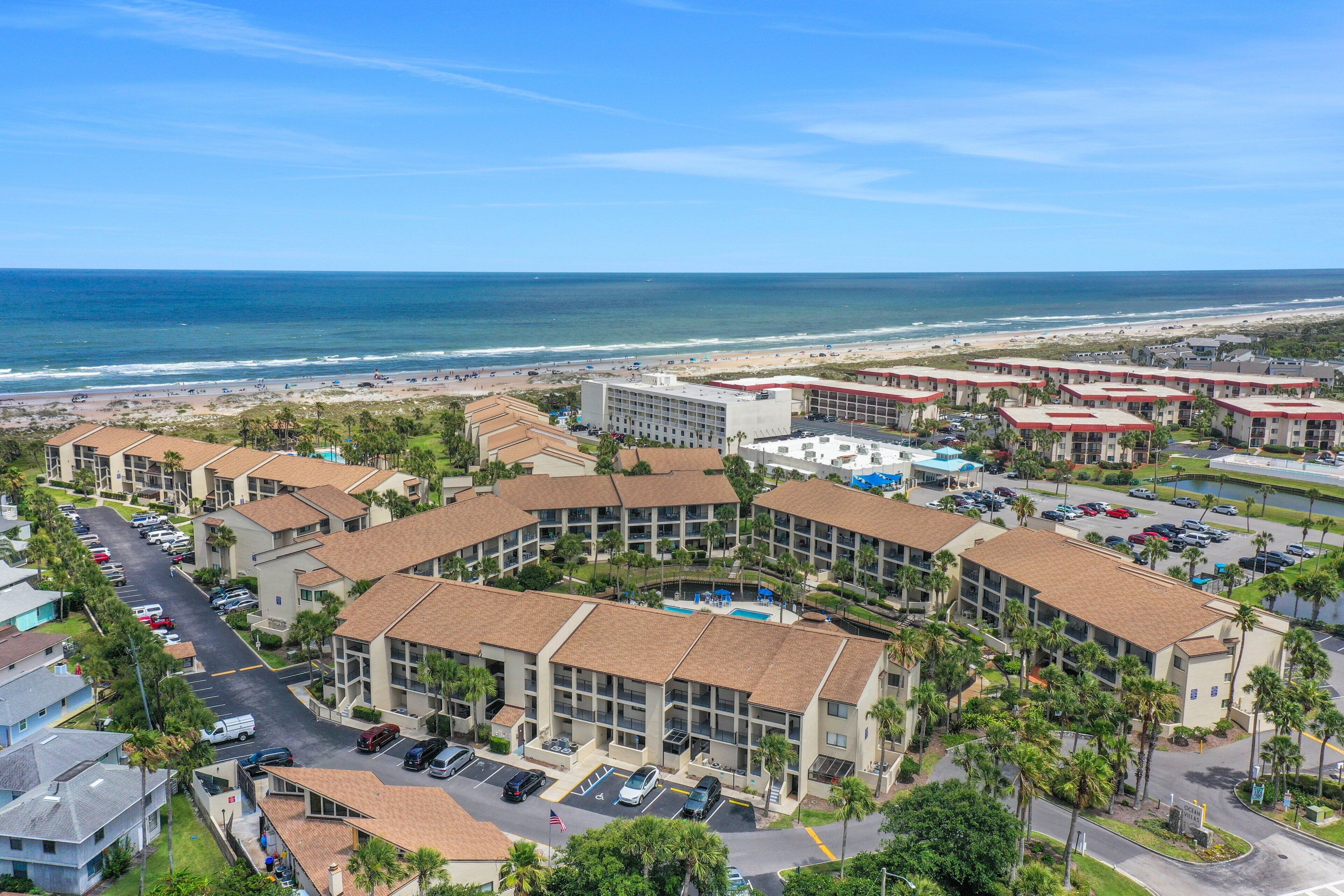 Een hotelcomplex aan de kust met meerdere gebouwen, een parkeerplaats en uitzicht op het strand.
