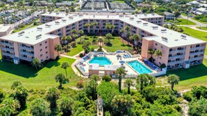 Ein mehrstöckiges Hotel mit Innenhof, der einen Swimmingpool, üppiges Grün und Palmen beherbergt.