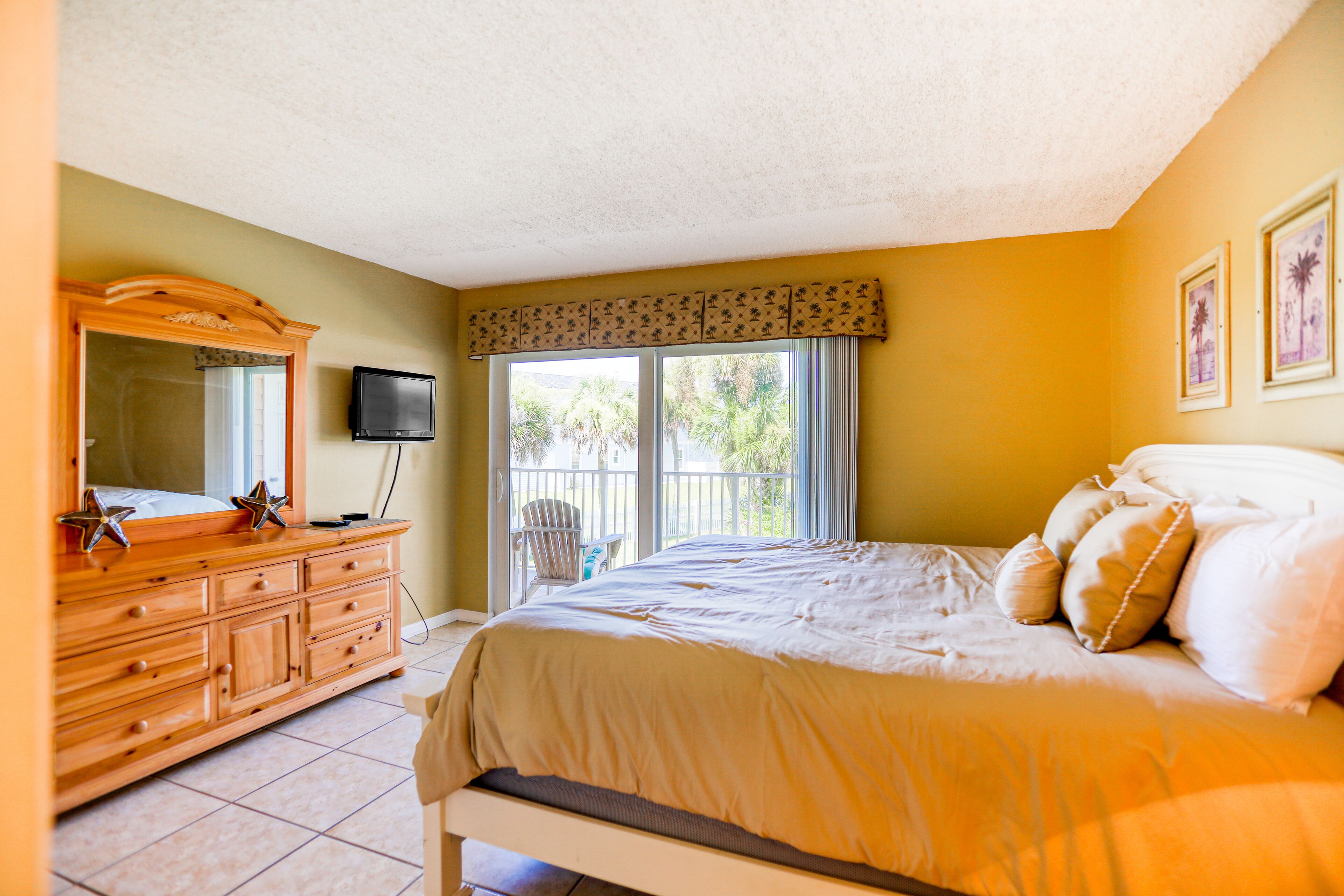 A bedroom with a bed, dresser, TV, and balcony.