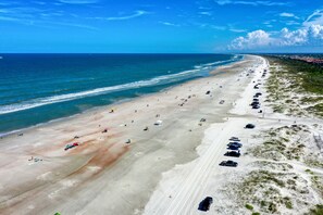 An aerial view of a beach with a long stretch of sand, a few umbrellas, and parked cars along the shore. - Ocean View Condo in Beachfront Resort With Wifi, Central AC, 2 Pools, & Tennis (St. Augustine)