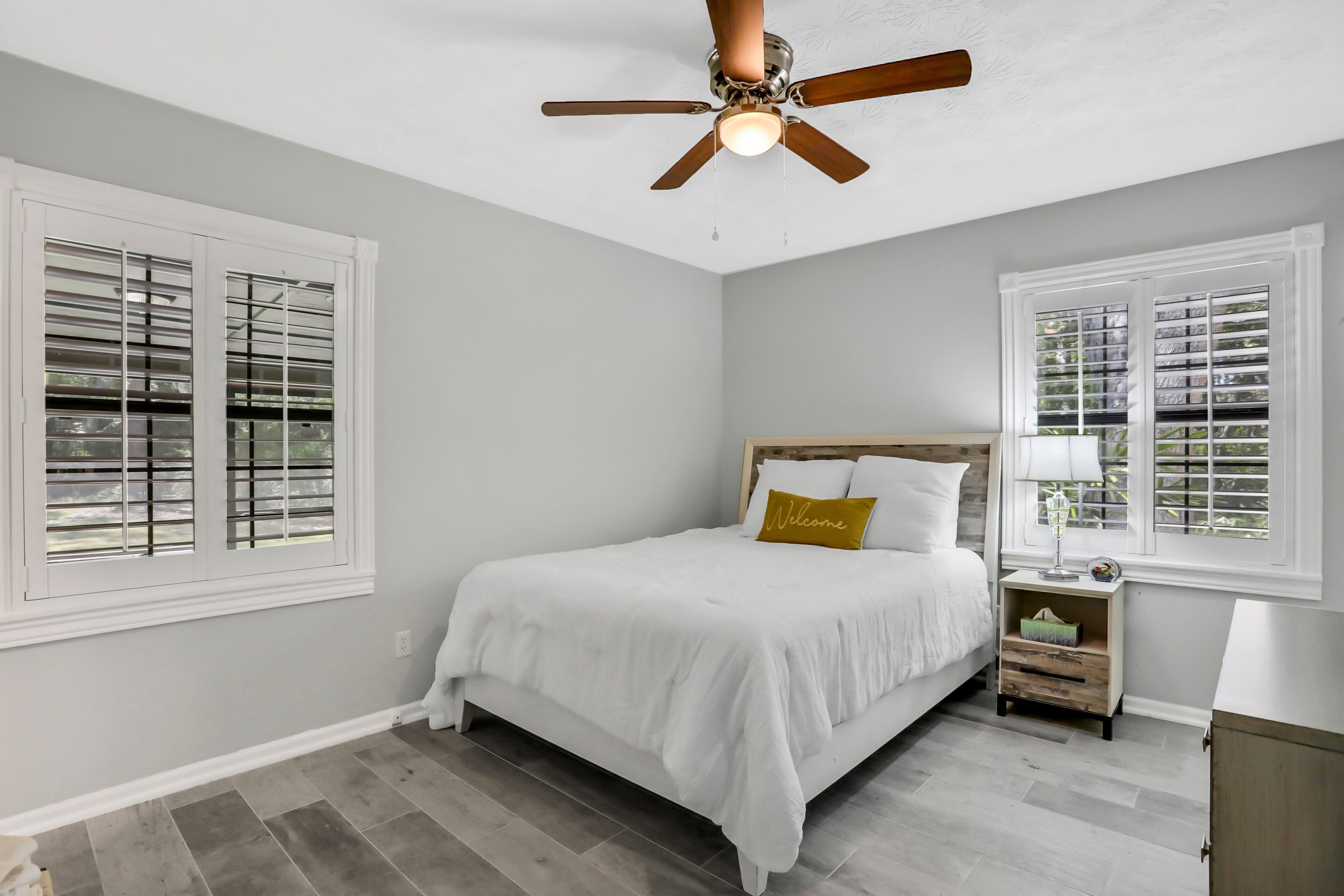 A bedroom with a bed, a nightstand, a ceiling fan, and two windows with blinds.