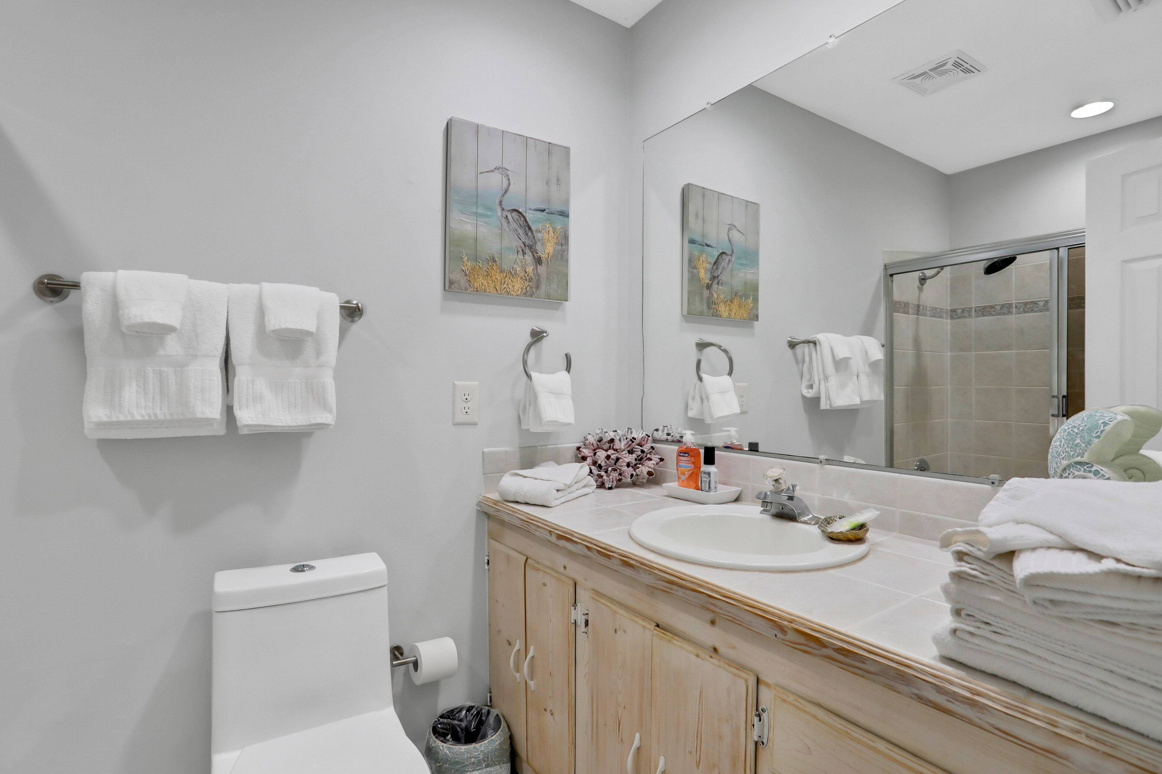 Een moderne badkamer met toilet, wastafel en douche. Handdoeken hangen aan de muur en er staat een prullenbak.