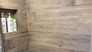 Eine Dusche mit Holzauskleidung und einem Regal mit Flaschen von Dove Shampoo und Conditioner.