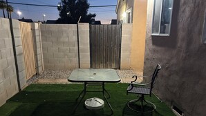 Eine Terrasse mit Tisch und Stuhl, umgeben von einer niedrigen Ziegelmauer und einem Holztor.