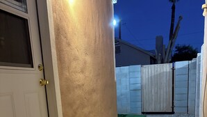 Ein Hausfassade im Dämmerlicht mit einer weißen Tür, einer beige strukturierten Wand und einem Holztor.