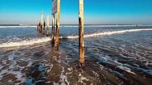 Une plage avec des poteaux en bois et un panneau dans l’eau.