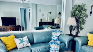 Un salon avec un canapé bleu, des coussins jaunes, une table basse en bois agrémentée d’objets décoratifs et une plante en pot.