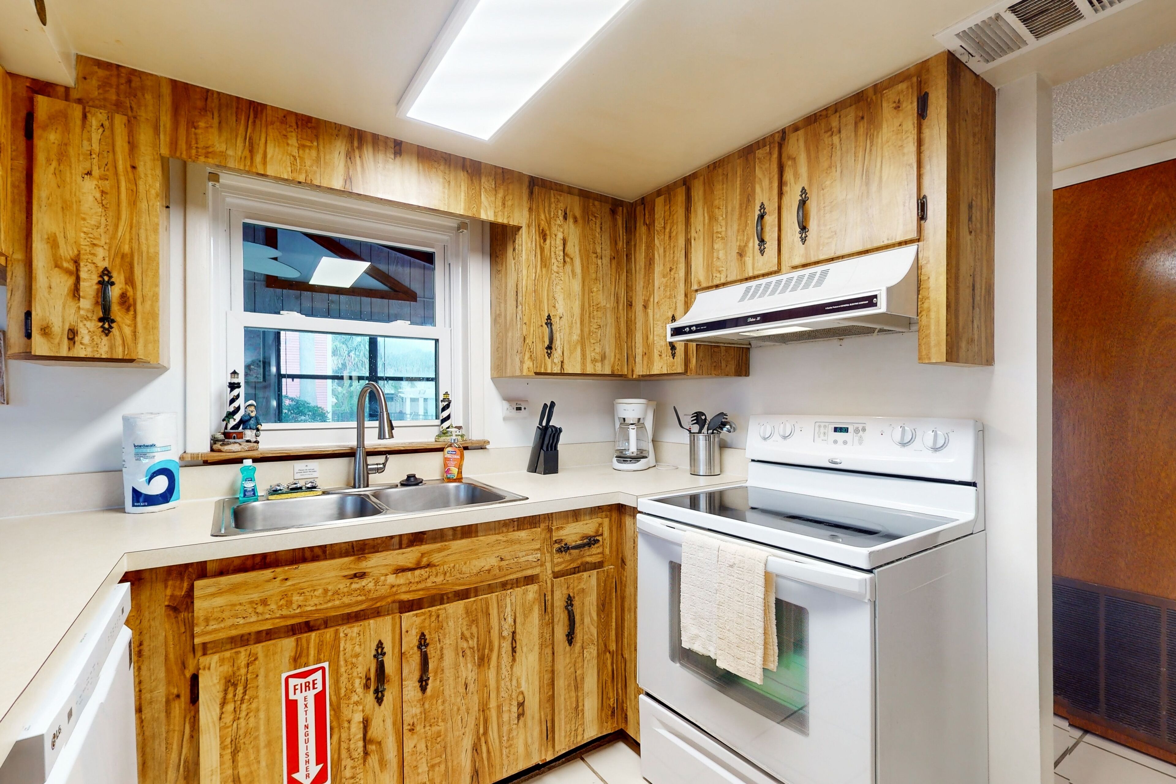 A kitchen with wooden cabinets, a white stove, a sink, and a window with a view of trees.