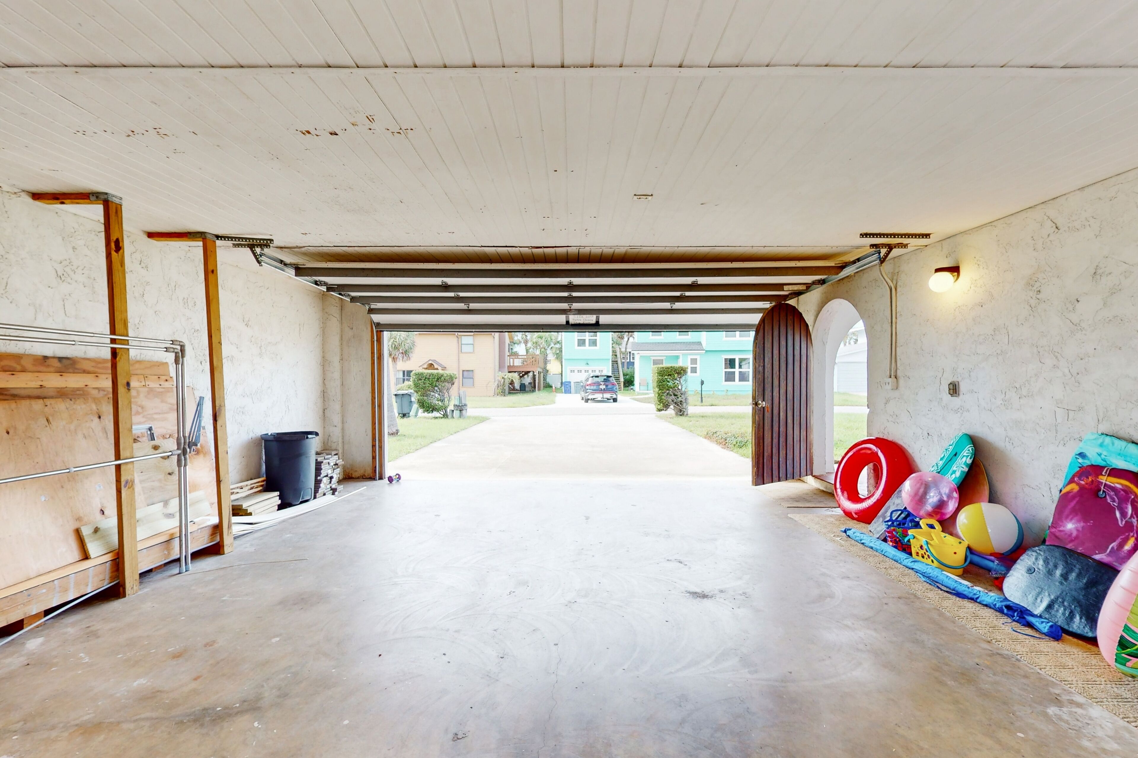 A garage with a concrete floor, wooden beams, and a view of a residential street.