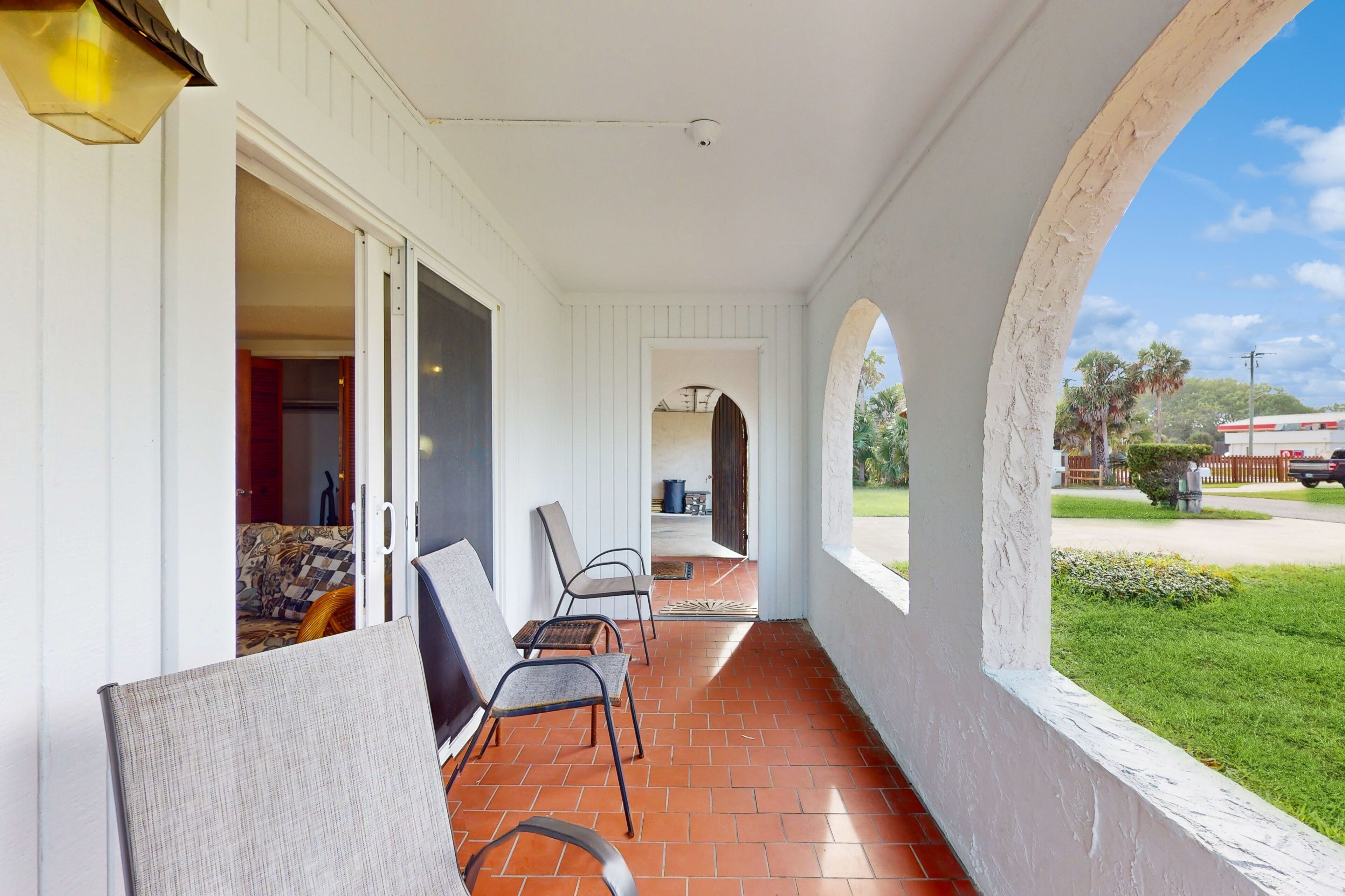 A covered porch with a brick floor, white walls, and a view of the street.