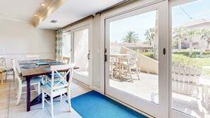 A dining area with a table and chairs, a blue mat, and a view of the outside patio with chairs and palm trees. - Snowbird Friendly, Oceanfront Community With Optional Golf Cart! (Fernandina Beach)