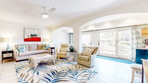 A spacious living room with a sofa, armchairs, a coffee table, and a large window offering a view of the outdoors. - Snowbird Friendly, Oceanfront Community With Optional Golf Cart! (Fernandina Beach)
