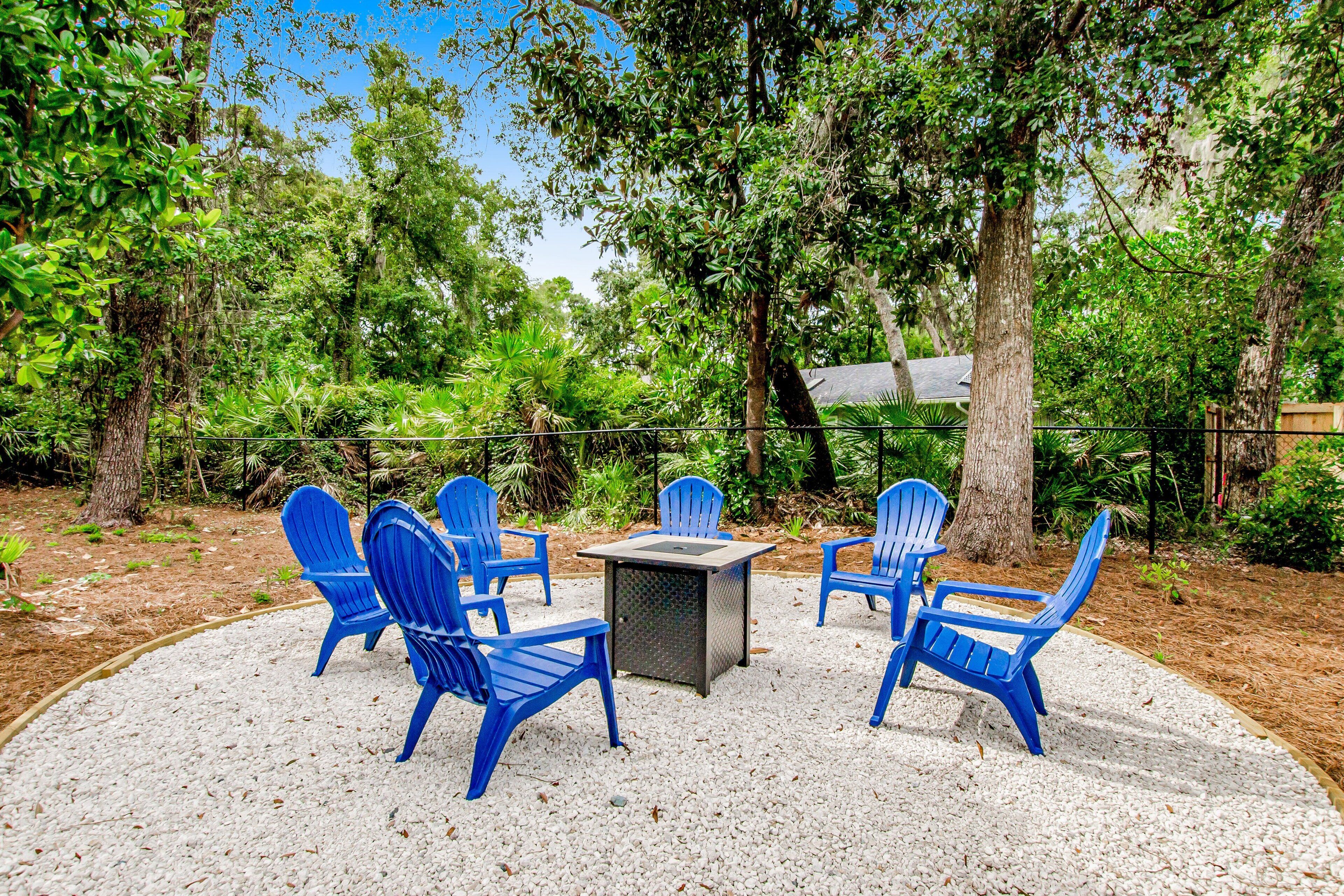 Een terras met blauwe stoelen en een vierkante tafel, omringd door grind, met op de achtergrond bomen en begroeiing.