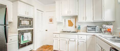 A kitchen with white cabinets, a brick floor, a refrigerator, an oven, a toaster, and a sink.