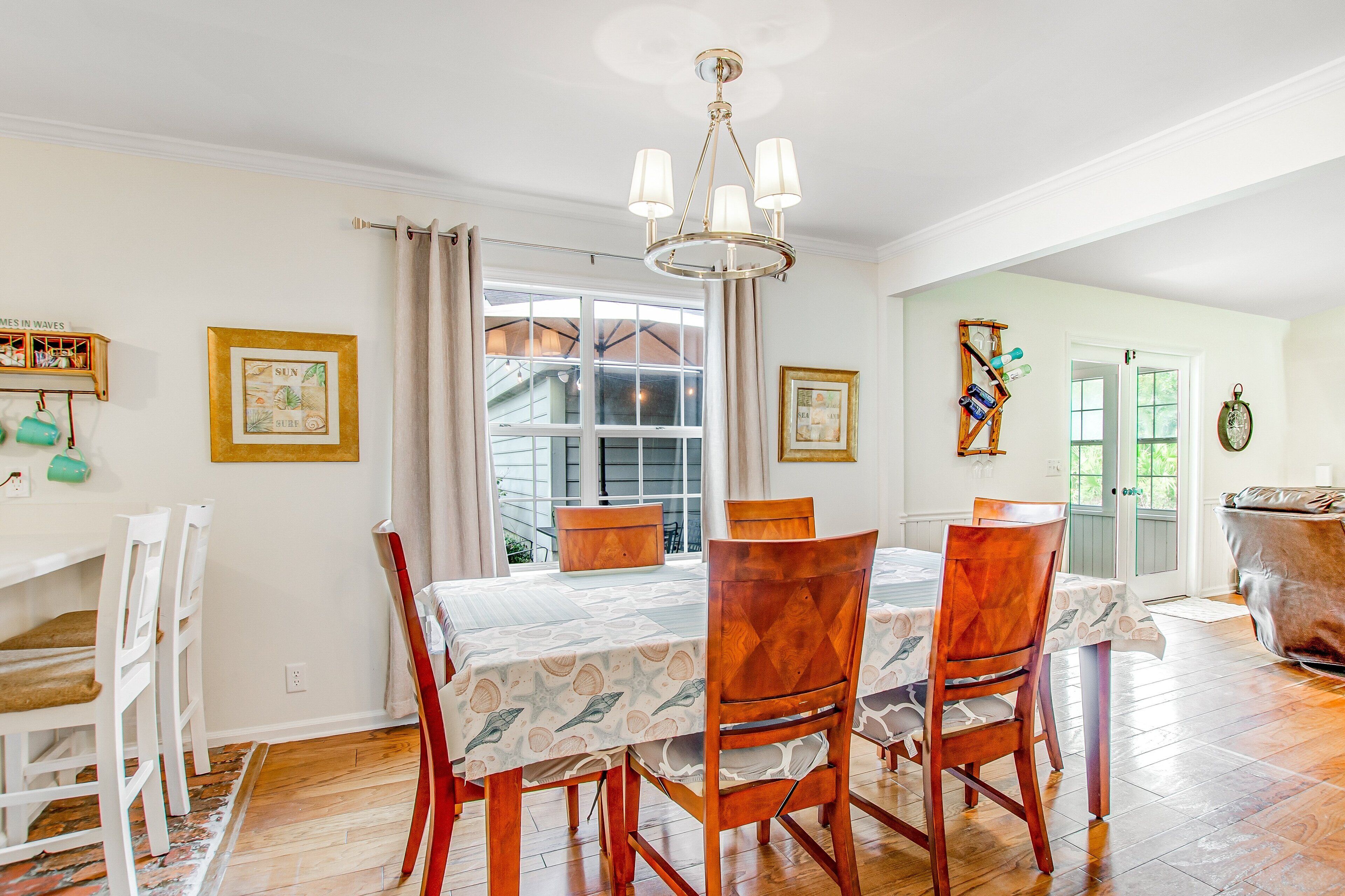 A dining area with a table set for four, wooden chairs, a chandelier, and a window with curtains.