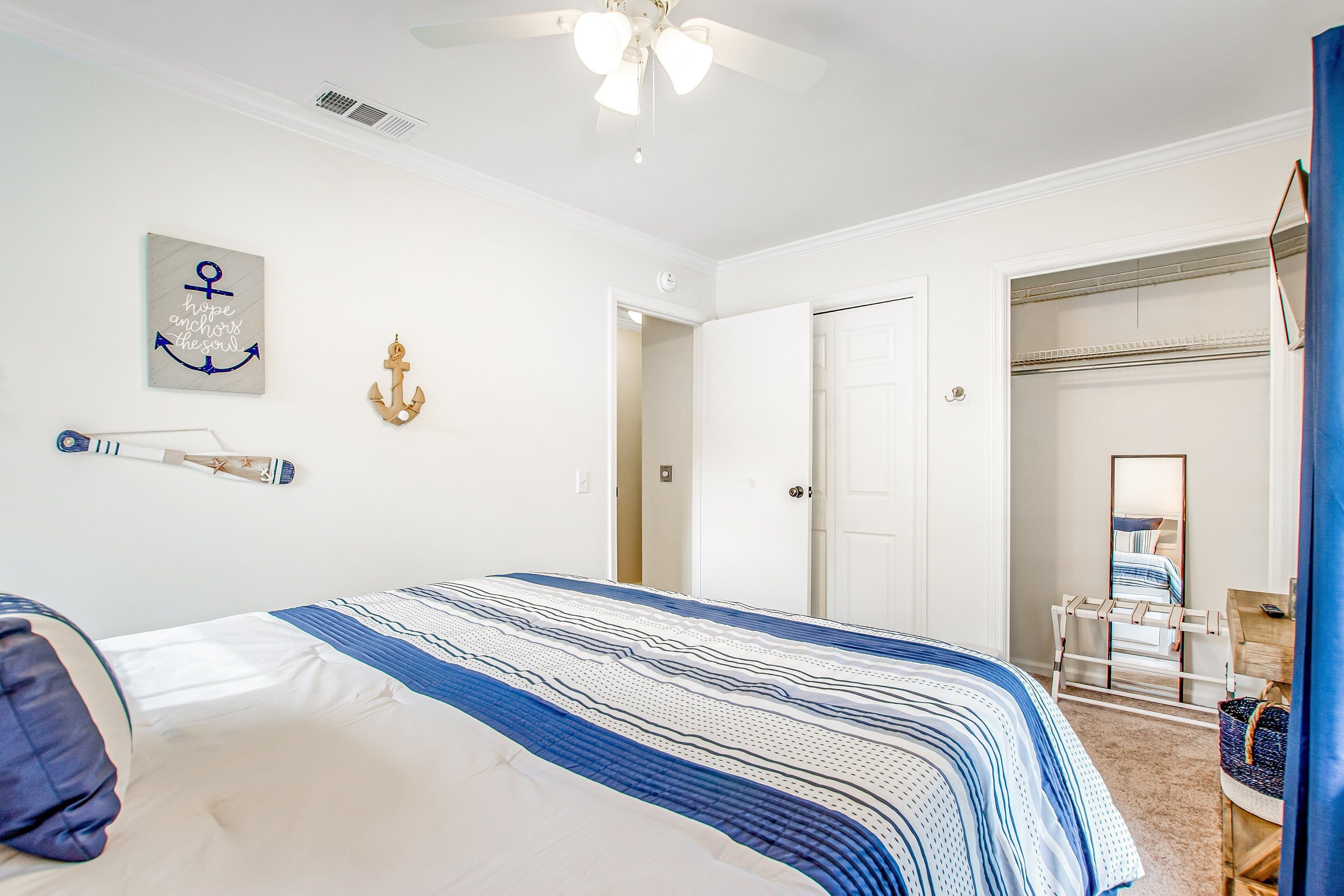 A bedroom with a bed, a ceiling fan, a door, and a small table with a chair.