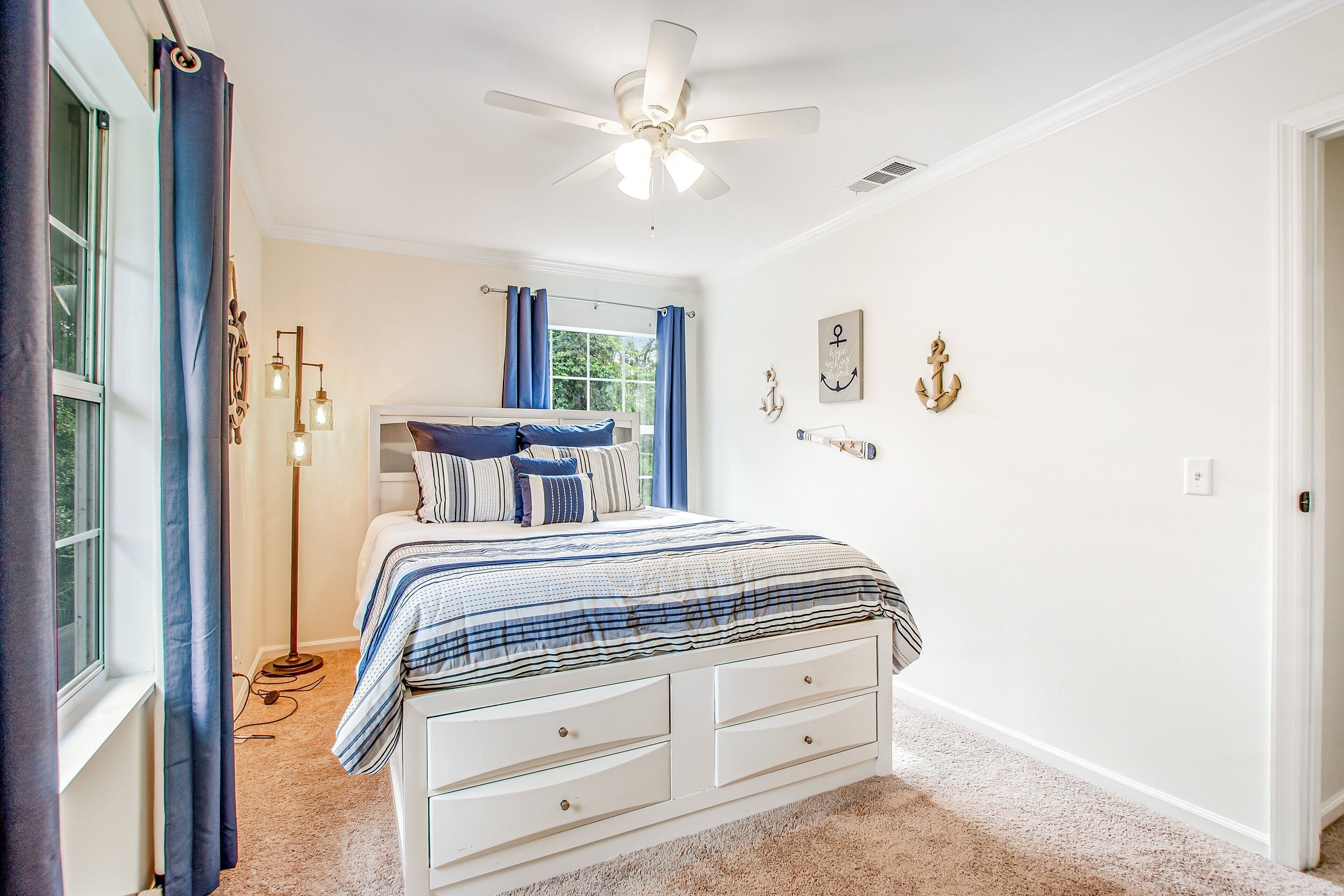 A bedroom with a bed, a ceiling fan, a window with curtains, and wall decorations.