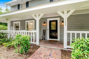 A two-story house with a white porch, a brick pathway, and a welcome sign. - Relaxing, Dog-friendly Home With Furnished Patio, Washer/dryer, Wifi, & AC (St. Simons Island)