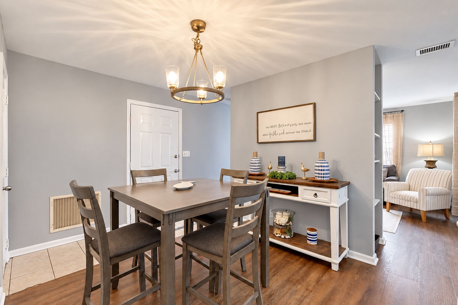 A dining area with a table, chairs, a chandelier, and a wall-mounted shelf with decorative items.