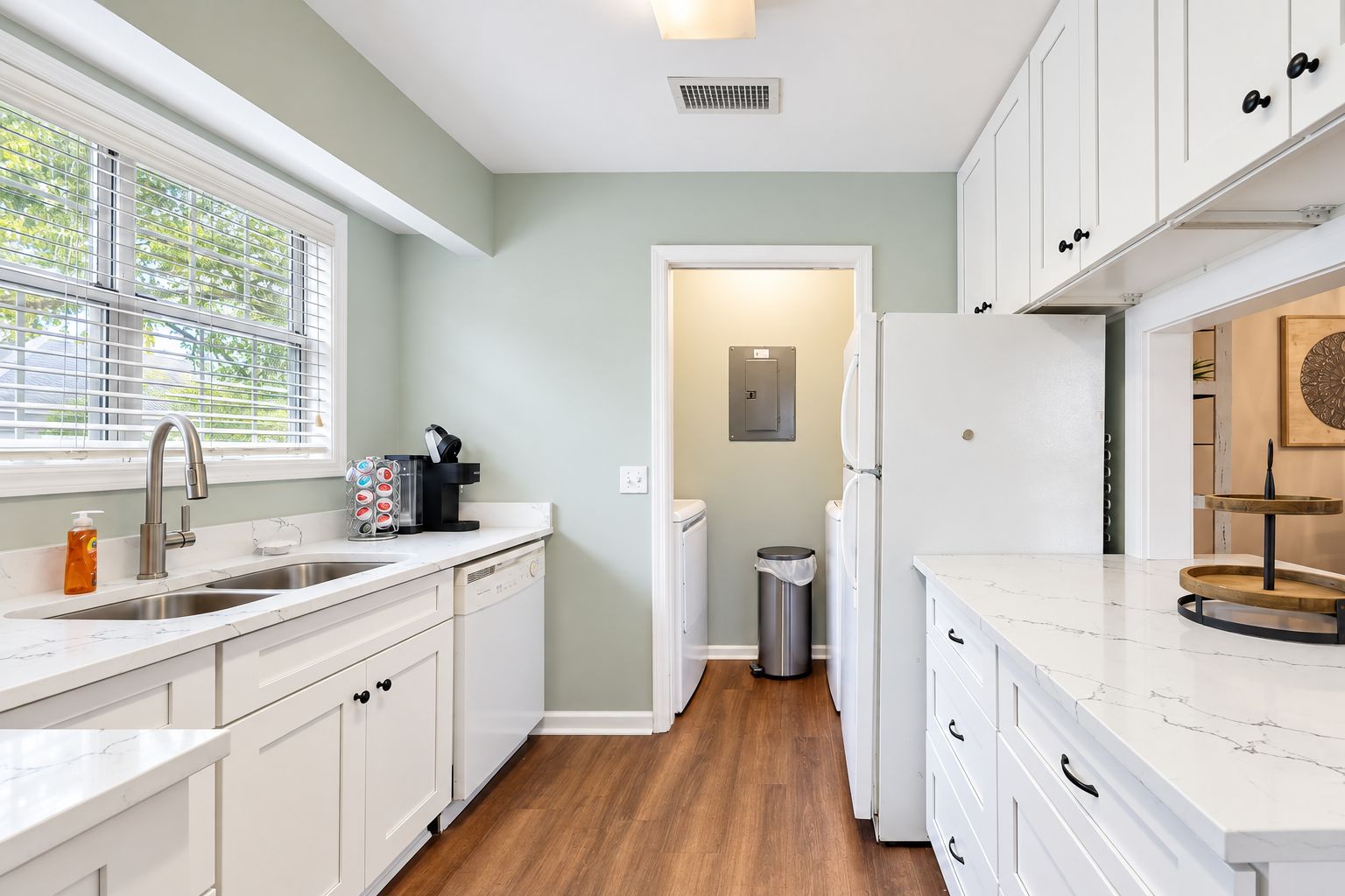 A modern kitchen with white cabinetry, a marble countertop, and a view of the outdoors through the window.