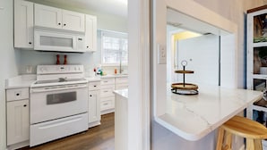 A modern kitchen with white cabinetry, a built-in microwave, a stove, and a marble countertop. - Private Retreat With Access to Community Pool & Nearby Entertainment (St. Simons Island)