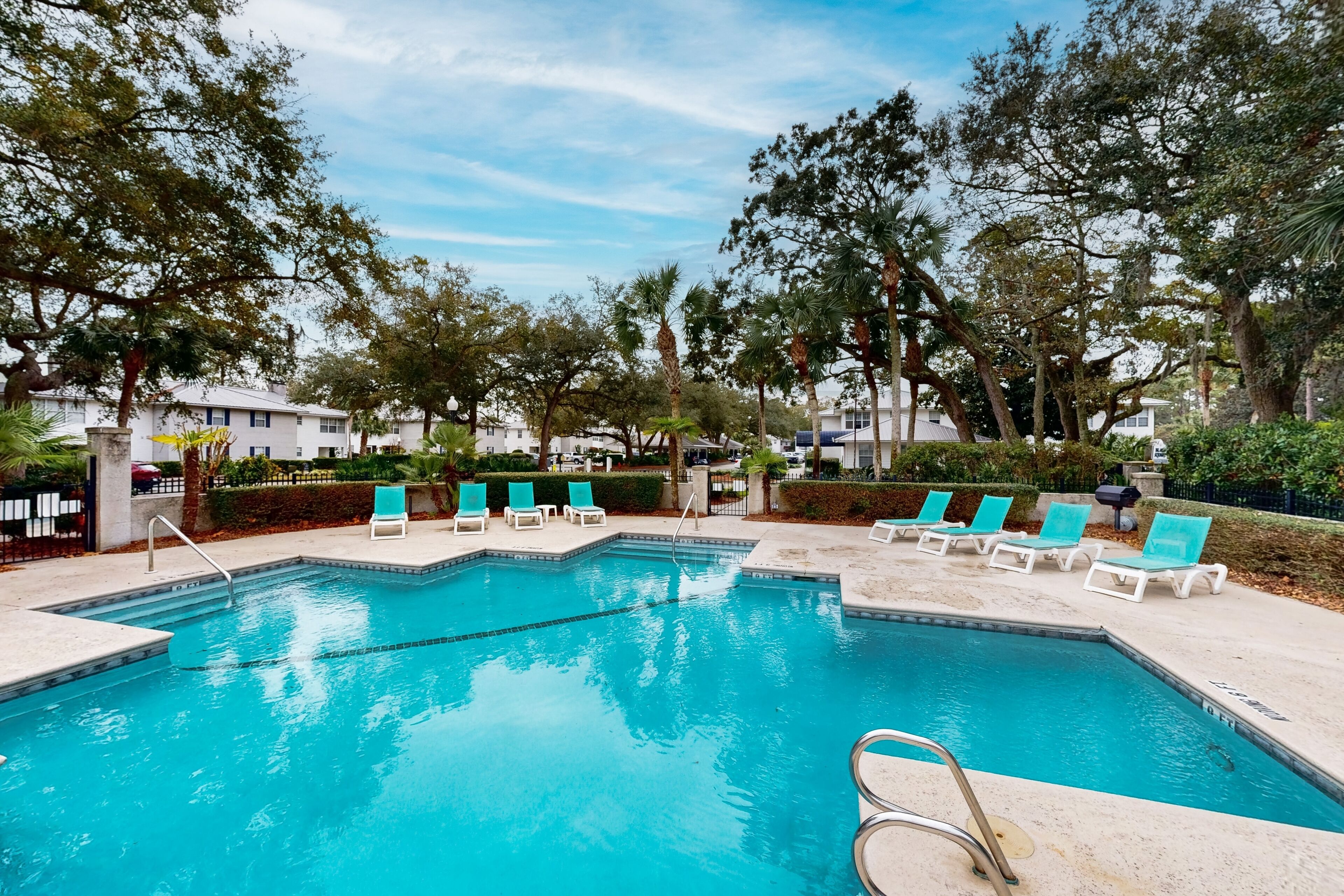 A rectangular swimming pool with clear blue water, surrounded by white lounge chairs and a paved deck.