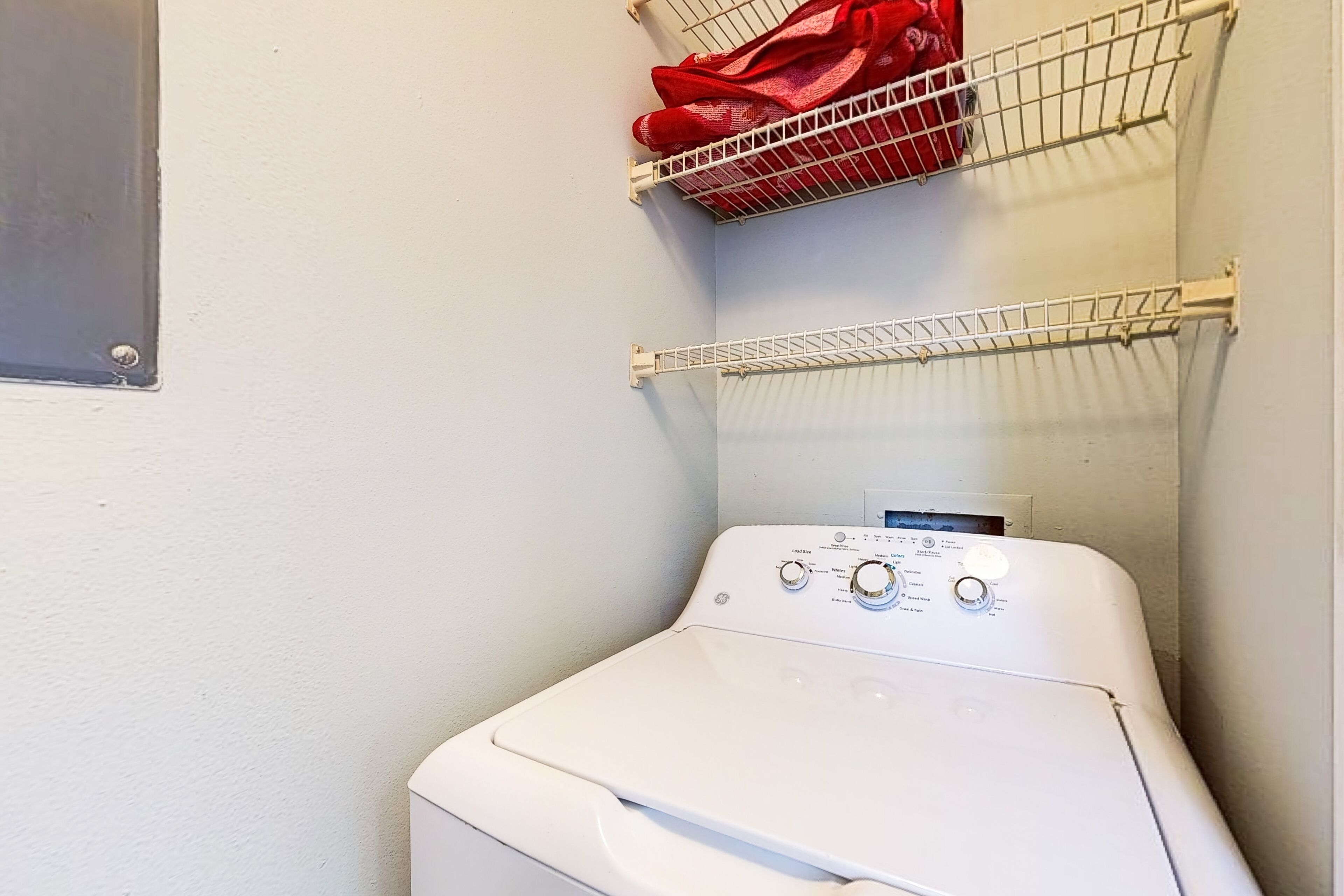 A laundry area with a white washing machine, two metal drying racks, and a red towel on the top rack.