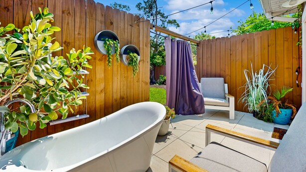 Un jardin avec une baignoire blanche, une clôture en bois et du mobilier d’extérieur.