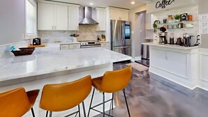 Une cuisine moderne avec des meubles blancs, un réfrigérateur en acier inoxydable et un îlot en marbre agrémenté de tabourets de bar.