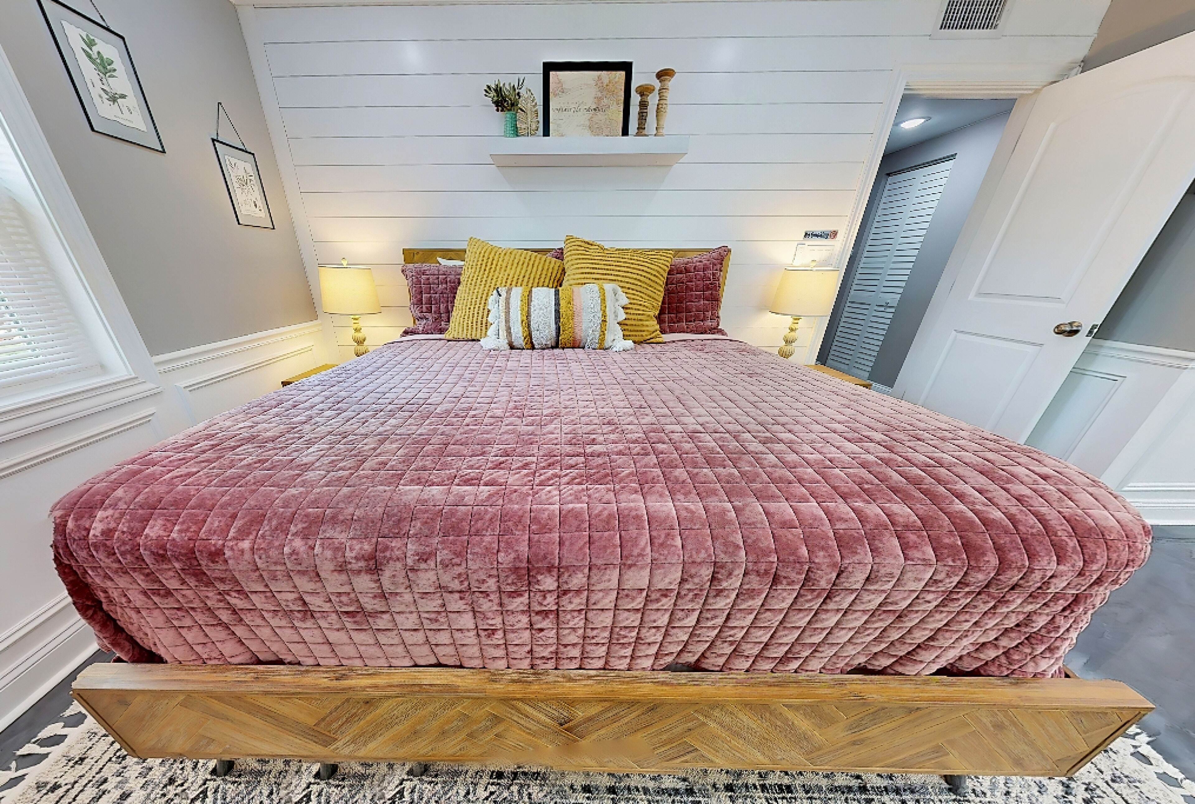 A bedroom with a large bed, a wooden headboard, and a white wall with a shelf above.