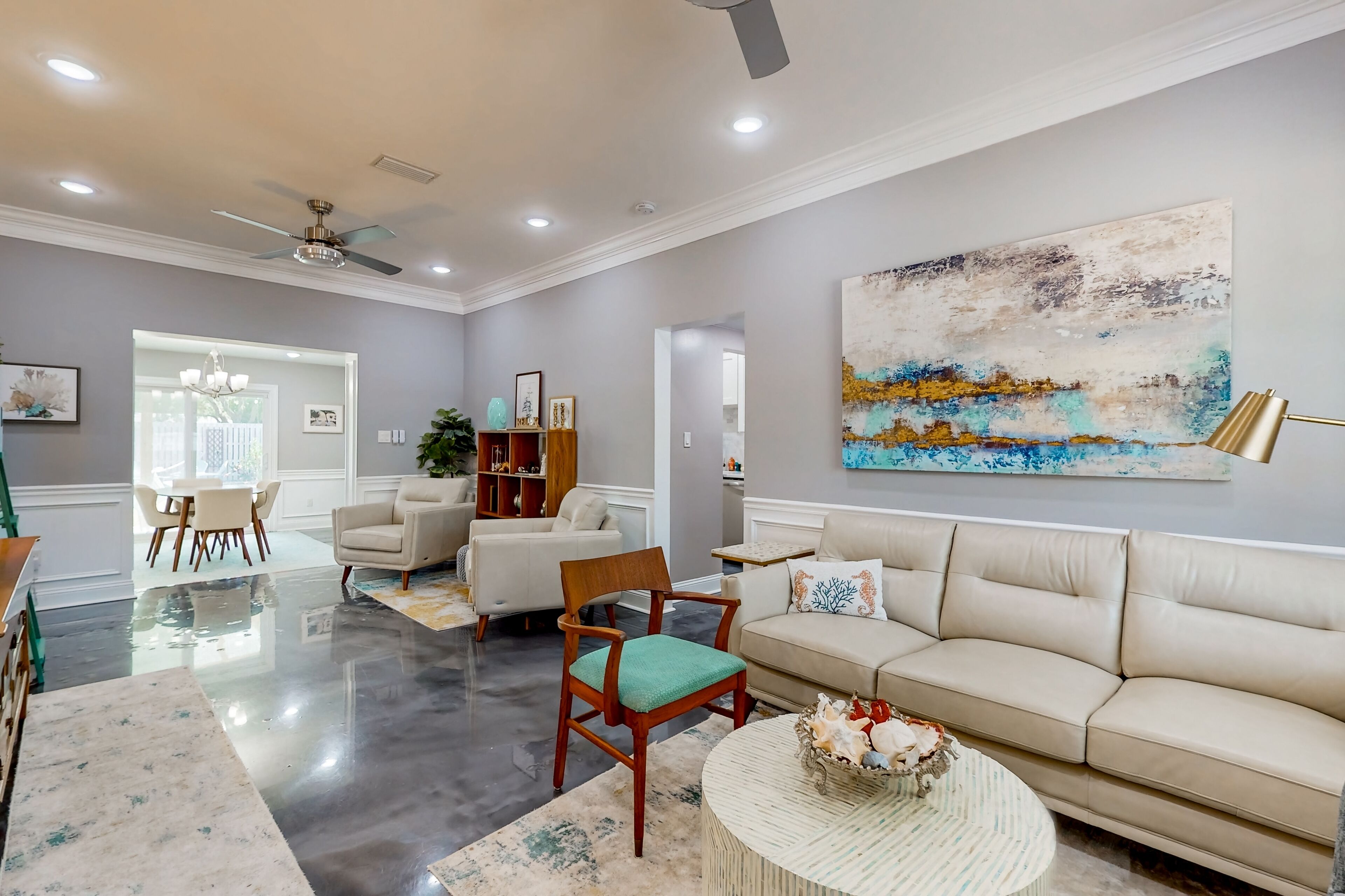 A spacious living room with a beige sofa, a wooden chair, a coffee table, and a painting on the wall.