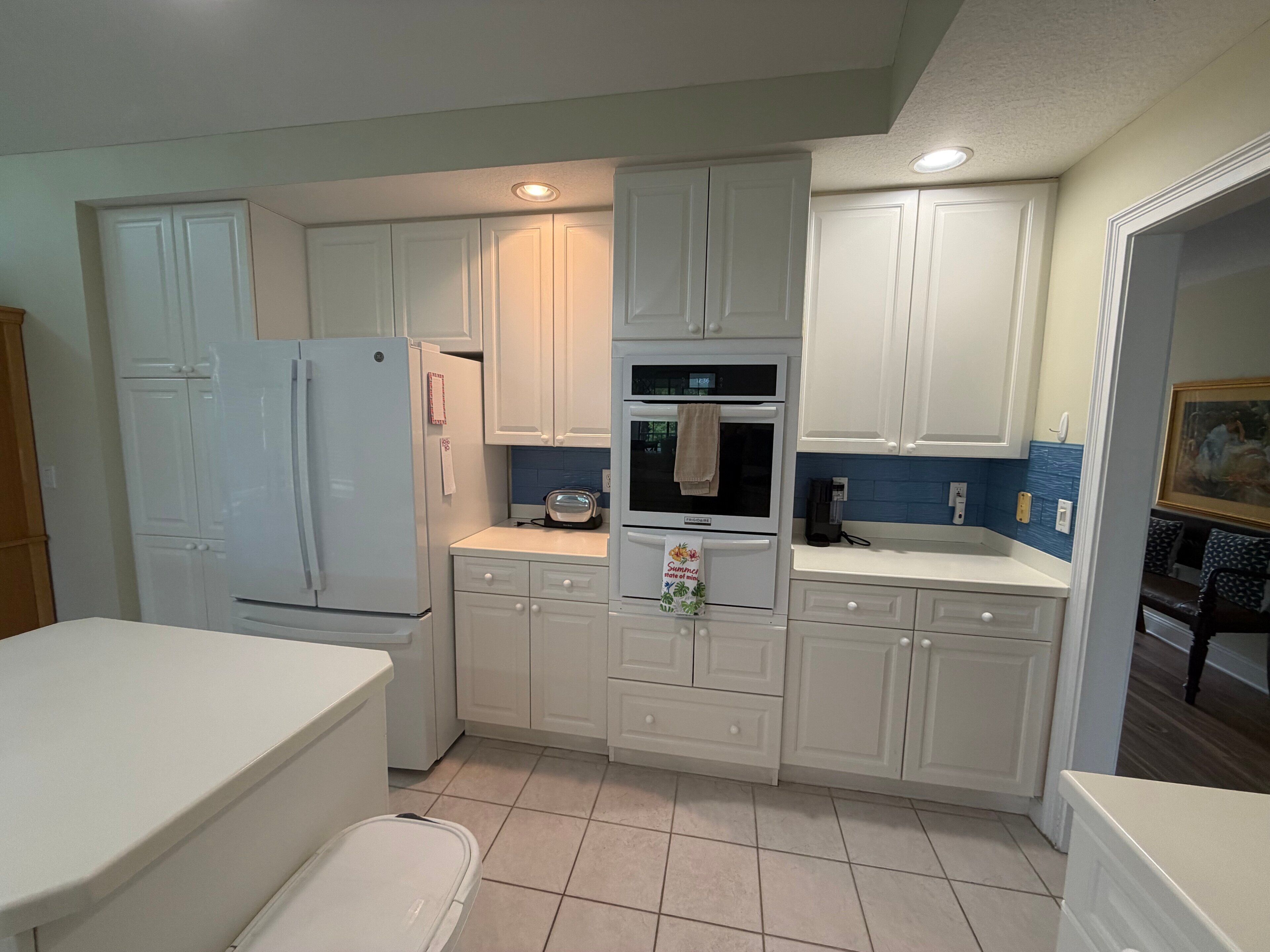 A kitchen with white cabinets, a refrigerator, an oven, and a sink.