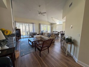 A spacious living room with a sofa, coffee table, and TV, a dining area with chairs and a table, and a ceiling fan. - Spacious Condo With Pool, hot tub and Private Washer/dryer (St. Augustine)