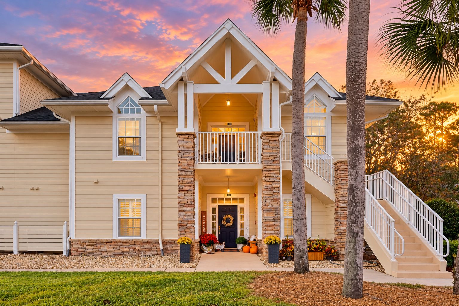 A two-story house with a balcony, a front porch with potted plants, and a staircase leading to the upper level.