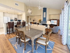 A spacious living area with a dining table, chairs, a sofa, and a television displaying a logo. - Spacious Condo With Pool, hot tub and Private Washer/dryer (St. Augustine)