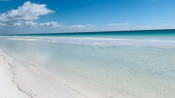 Een strand met helder turquoise water en wit zand.