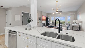 Een moderne keuken met een dubbele spoelbak, witte kasten en een eethoek met uitzicht.