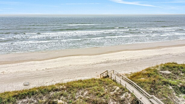 Une plage avec une promenade en bois menant au rivage, une plage de sable et des vagues de l’océan.