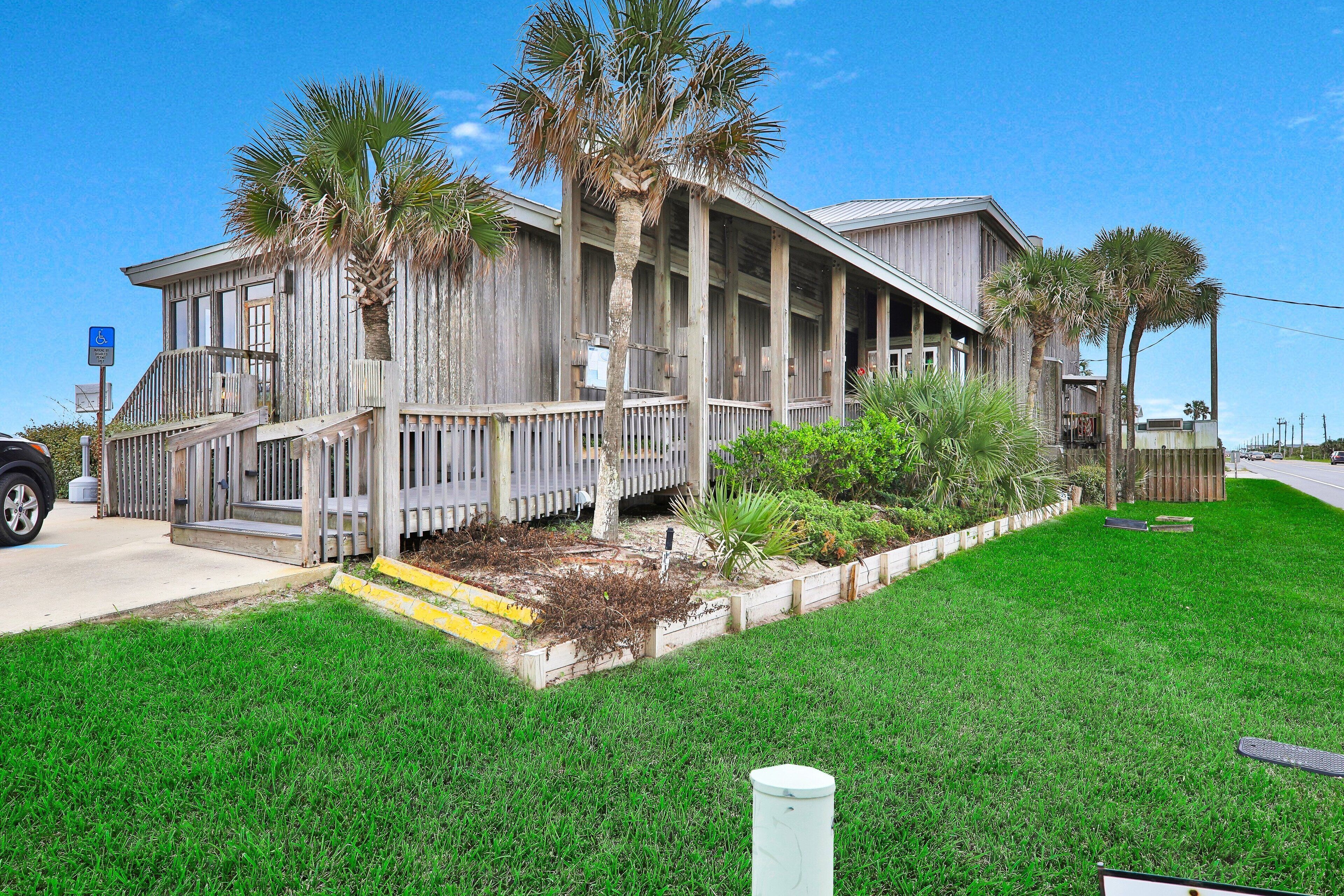 A wooden building with a porch, palm trees, and a grassy yard.