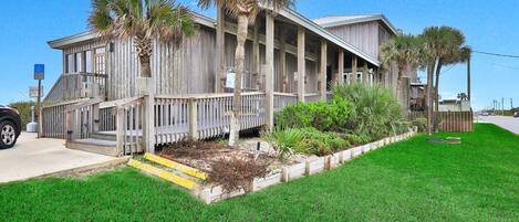 A wooden building with a porch, palm trees, and a grassy yard.