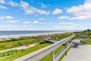A wooden boardwalk leading to a beach with a clear view of the ocean and a grassy area with steps and railings. - Renovated Condo With Balcony, Lush Views, Outdoor Pool (Fernandina Beach)