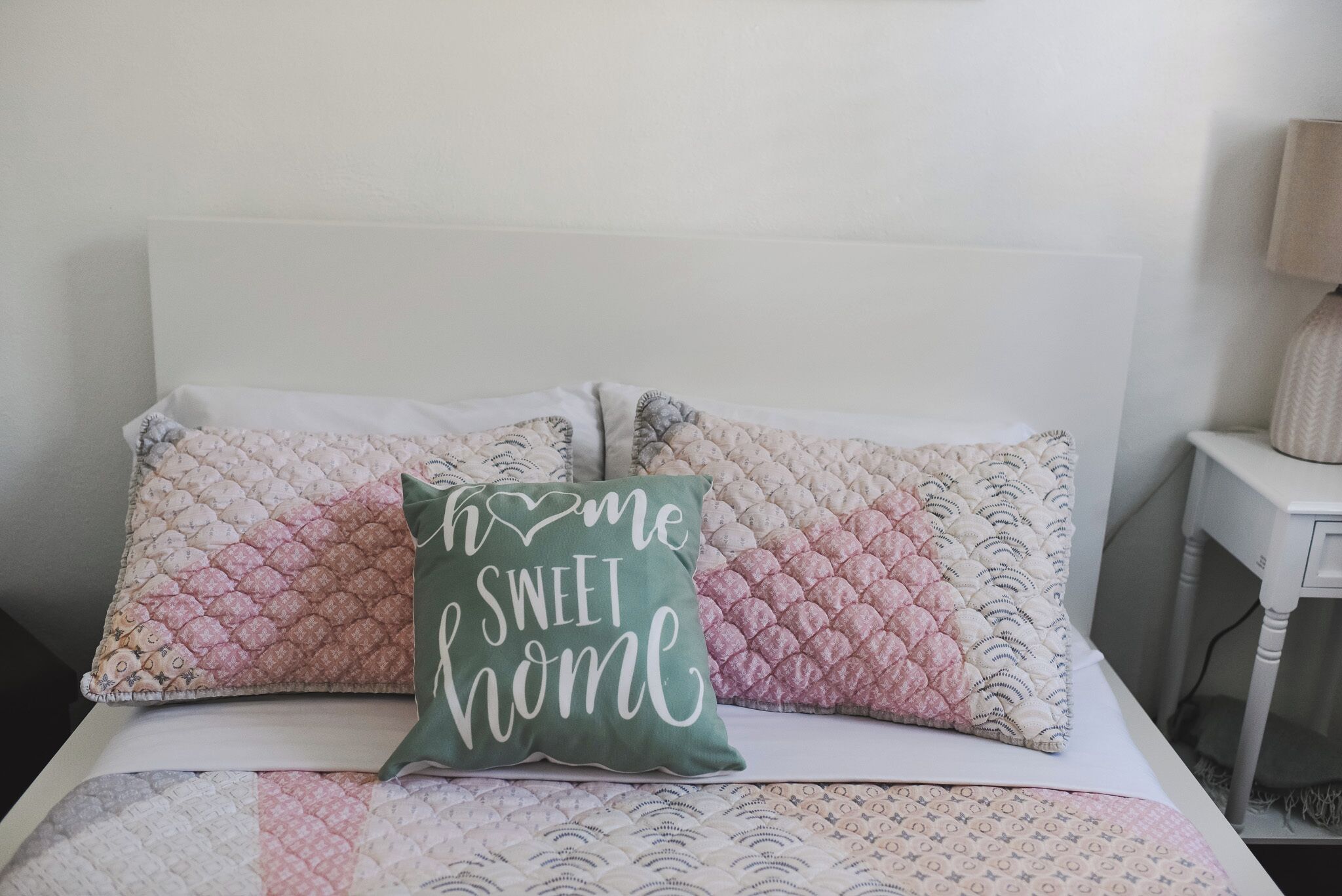 Una cama con una colcha acolchada y dos almohadas, una con un cojín verde y la otra con un cojín rosa.