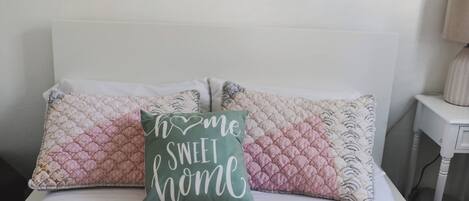 Una cama con una colcha acolchada y dos almohadas, una con un cojín verde y la otra con un cojín rosa.