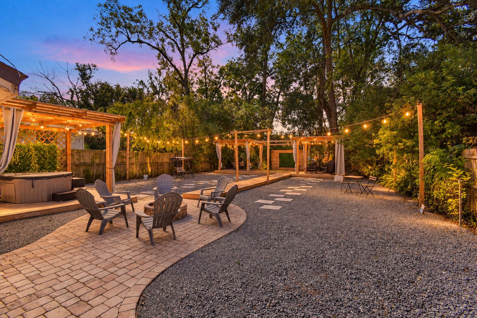 An outdoor patio area with seating and a hot tub, surrounded by trees and string lights.
