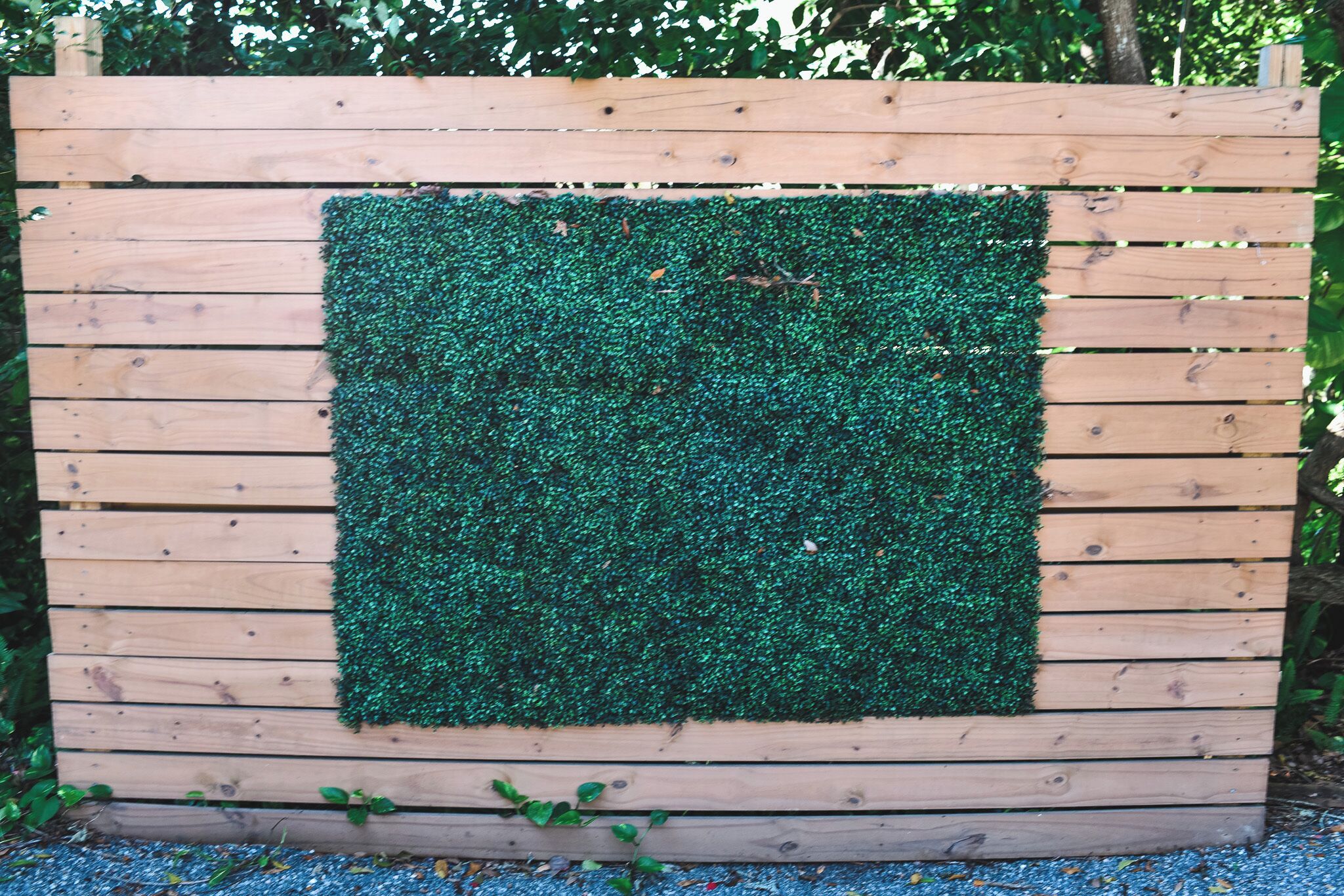 Una valla de madera con un panel cuadrado cubierto de césped artificial verde.