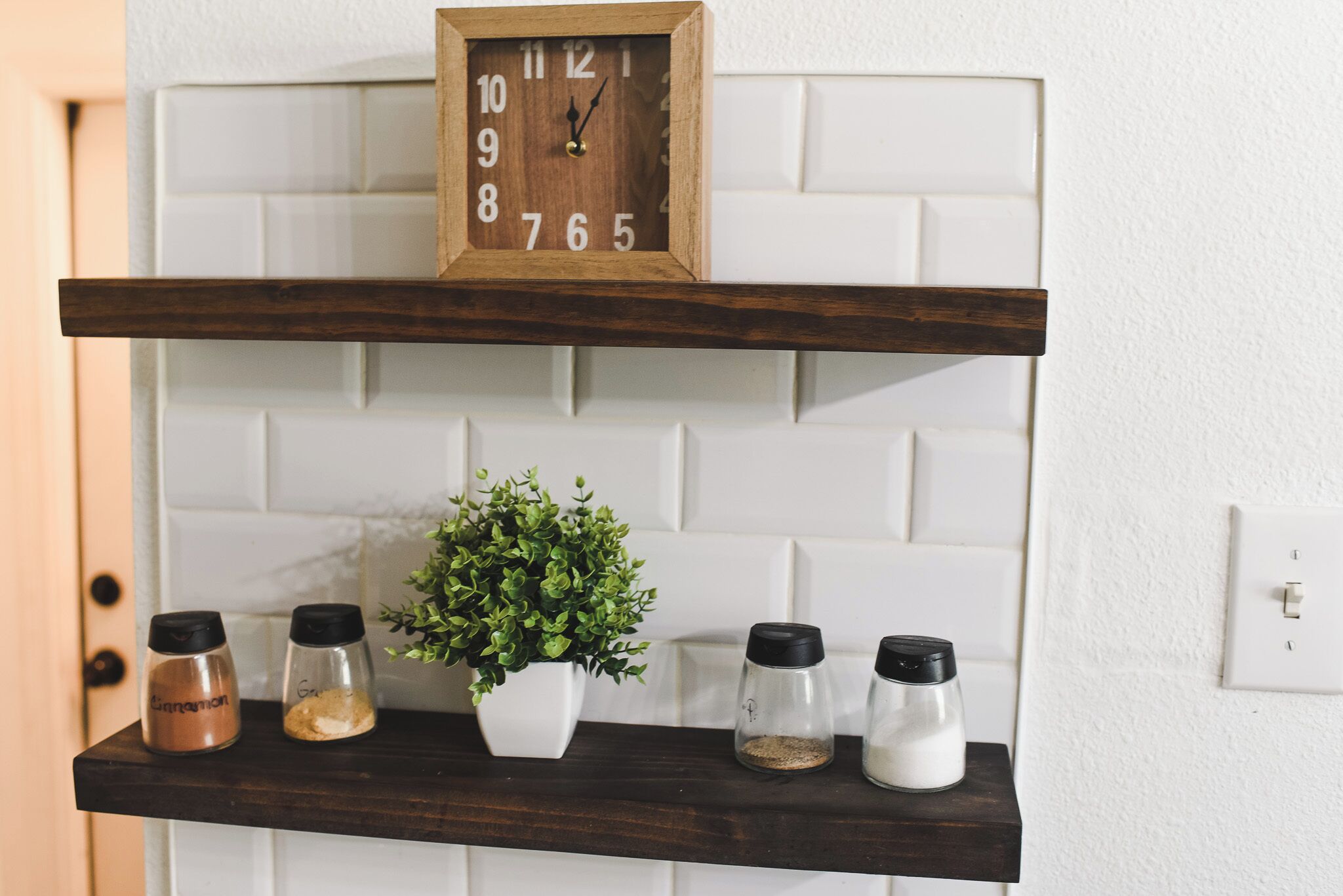 A kitchen shelf with a clock, salt shakers, pepper shakers, and a potted plant.