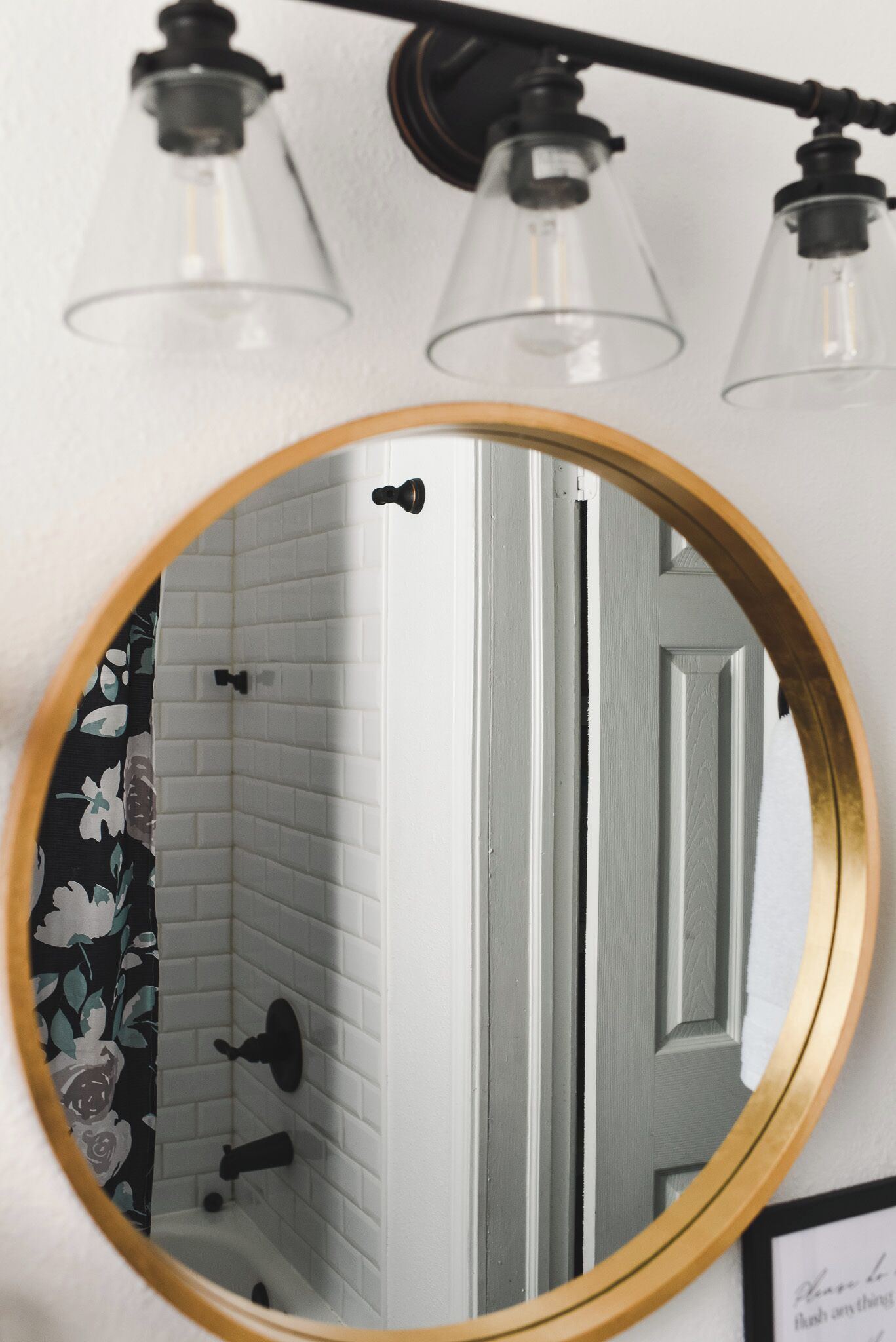 A bathroom with a round mirror, white tiled walls, a shower, and a black faucet.