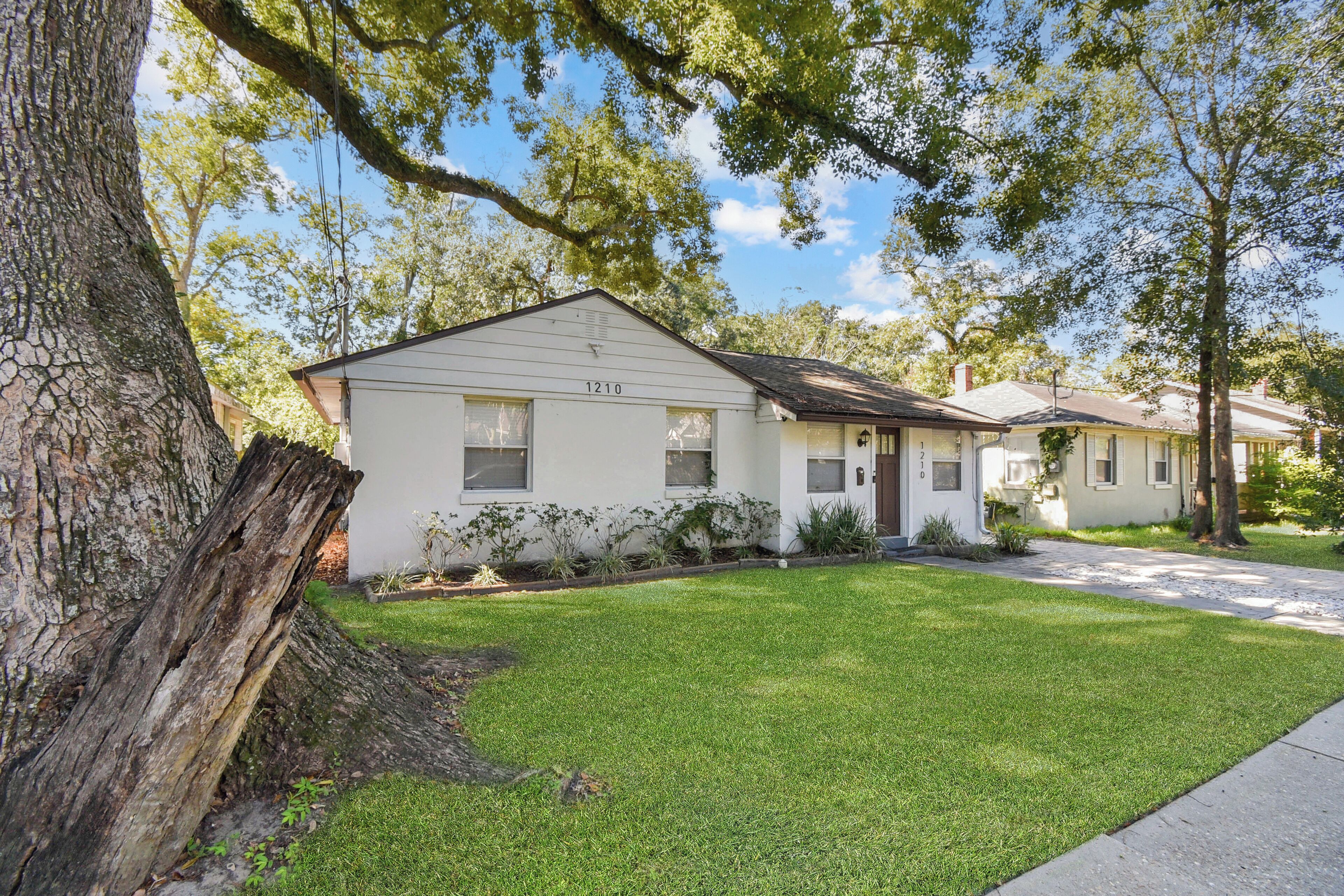 A single-story house with a number 1210 on the front, surrounded by a well-maintained lawn and trees.